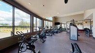This modern fitness center, located in Beaverton, Oregon, offers a comprehensive workout environment designed to support a wide range of exercise routines. The space is spread across a single floor and benefits from an abundance of natural light, courtesy of expansive floor-to-ceiling windows that line the perimeter walls and offer views of the surrounding neighborhood and greenery.

The cardio zone is well-stocked, featuring a row of spin bikes, treadmills, elliptical trainers, and stair climbers — all positioned to take advantage of the outdoor views. Wall-mounted TVs provide entertainment during cardio sessions. A large mirrored wall enhances the sense of space and allows users to monitor their form.

The functional fitness area includes a rack of stability balls in multiple sizes, resistance bands, medicine balls, dumbbells, and exercise mats, catering to flexibility and bodyweight training. A multi-station cable machine provides versatility for strength training.

Ceiling fans and recessed lighting contribute to a comfortable and well-ventilated atmosphere throughout. The flooring is a durable, cushioned material suited for high-impact activity. Motivational wall art adds an energetic aesthetic to the space. The overall design is clean and contemporary, creating an inviting environment for users of all fitness levels.