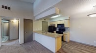 This single-floor residence offers a well-organized layout that balances open communal spaces with comfortable private areas. The heart of the home is an open-concept kitchen and living area, where a peninsula-style counter with a granite-look surface and an integrated sink serves as the central divide. The kitchen is equipped with black appliances, including a refrigerator, electric range, and over-the-range microwave, complemented by light wood cabinetry and a mosaic tile backsplash. Hardwood-style flooring runs throughout the kitchen, transitioning to plush carpet in the adjoining living area. The living room features a ceiling fan with a light fixture, a fireplace, and direct sightlines to the front entry door. The bedrooms are carpeted and each include a ceiling-mounted light fixture and a closet, with one bedroom offering a walk-in closet and a window overlooking a green outdoor view. The hallway leading to the bedrooms features hardwood-style flooring and connects to a bathroom with a granite-look vanity countertop and wood cabinetry. Textured ceilings are consistent throughout, adding a classic character to the space.