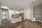Located at 8465 Regents Rd in San Diego, CA, this one-bedroom, one-bathroom residence offers a well-designed, single-floor layout that makes efficient use of its space. The open-concept living and kitchen area serves as the heart of the home, featuring rich hardwood-style flooring, recessed lighting, and neutral-toned walls that create a clean, modern aesthetic. The kitchen is outfitted with white cabinetry, granite countertops, stainless steel appliances including a refrigerator, range, microwave, and dishwasher, and a peninsula island that provides additional prep space and separates the kitchen from the living area. The living room is bathed in natural light and opens directly onto a private balcony through a sliding glass door, offering outdoor views of the surrounding landscaping. The bedroom features soft carpeting, a ceiling fan, a natural light window with blinds, and access to a dedicated closet. The bathroom is finished with a white vanity featuring granite countertops, a tub-shower combination with tile surround, and wood-style flooring that ties cohesively to the rest of the unit. Overall, the space presents a practical and comfortable living environment with modern finishes throughout.