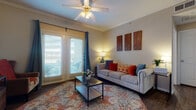 This single-floor residence offers a thoughtfully designed layout that balances comfort and functionality across its key living spaces. The living room serves as the centerpiece of the home, featuring crown molding, a ceiling fan with integrated lighting, and rich dark hardwood-style flooring. Large French doors with horizontal blinds and teal curtain accents allow generous natural light to pour in, creating a warm and inviting atmosphere. Decorative wall art panels and a glass-top coffee table complete the well-styled space.

The galley-style kitchen is efficiently organized with light wood cabinetry lining both sides, offering ample storage and counter space. Light-toned countertops complement the wood-style flooring, and white appliances including a range, refrigerator, and dishwasher provide all essential functionality.

The bedrooms are carpeted and serene, each benefiting from natural light through shuttered windows. One bedroom includes a walk-in closet with built-in hanging space, while both rooms offer a calm, restful ambiance with neutral wall tones.

The bathroom features light wood cabinetry with a spacious vanity, a tiled shower-tub combination, dark hardwood-style flooring, and recessed lighting, contributing to a clean and practical finish throughout.