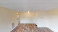 Located in Cumberland, Indiana, this single-story home offers a straightforward, functional layout finished with consistent wood-look flooring throughout. The main living area is open and well-proportioned, featuring light neutral walls, flush-mount ceiling lighting, and a textured ceiling. A wall-mounted thermostat and a floor-level heating unit are also present, adding to the practicality of the space.

The bedrooms each feature the same durable wood-look flooring, textured ceilings, and neutral wall tones. Both rooms include sliding-door closets with louvered panels and windows that allow natural light in while offering views of the surrounding greenery and neighborhood. The rooms feel comfortable and versatile for various furnishing arrangements.

The kitchen is equipped with white cabinetry extending to the ceiling, offering generous storage. A stainless steel gas range with a built-in oven serves as the centerpiece, complemented by light-colored countertops and an under-cabinet range hood. The wood-look flooring continues here, tying the space together cohesively.

The bathroom features a clean, white tub-shower combination with a molded surround and a chrome showerhead and faucet. The overall aesthetic of the home is clean, neutral, and move-in ready.