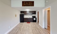 This single-floor unit offers a clean, functional layout with consistent light wood-tone flooring and a neutral color palette throughout. The living area is bright and open, benefiting from a large window that brings in natural light, and is equipped with a wall-mounted HVAC unit for year-round comfort. The space flows naturally into the rest of the unit through wide, well-framed doorways.

The kitchen is efficiently designed with rich dark-stained cabinetry providing ample storage, a light-toned countertop with an integrated sink, and a full suite of black appliances including a refrigerator and electric range. Overhead, a flush-mount ceiling fixture ensures well-lit meal preparation.

The bedroom features a ceiling fan with light, a built-in closet with a hanging rod, and direct sightlines to the kitchen, reinforcing the unit's connected layout. The full bathroom includes a single-sink vanity with dark cabinetry, a framed mirror, wall sconce lighting, and a shower-tub combination. An adjacent linen-style shelving unit adds practical storage.

A dedicated utility room houses the water heater and electrical panel, keeping mechanical systems organized and accessible. Textured ceilings are present throughout, and clean white baseboards frame every room, contributing to a tidy, move-in-ready presentation.