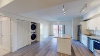 This well-appointed single-floor unit offers a thoughtfully designed open-concept layout that seamlessly connects the kitchen and living areas. The kitchen is a standout feature, showcasing crisp white shaker cabinetry, granite countertops, a central island for additional prep and seating space, stainless steel appliances including a refrigerator, electric range, microwave, and dishwasher, and track lighting overhead. Light wood-tone flooring flows throughout the main living areas and bedrooms, lending a warm, cohesive aesthetic.

The living area is bright and airy, benefiting from natural light and direct access to a generous private balcony. The balcony features exposed brick-textured walls and open views of surrounding greenery, providing a comfortable outdoor retreat. In-unit stacked washer and dryer are conveniently tucked behind louvered closet doors within the main living space.

The bedrooms are well-proportioned, each featuring ceiling fans, wood-tone flooring, and windows with blinds that frame outdoor views. Two bathrooms serve the unit: one features a full soaking tub with tiled surround and granite vanity, while the other offers a glass-enclosed walk-in shower and a wide granite-topped vanity with a large mirror. The overall ambiance is clean, modern, and move-in ready.