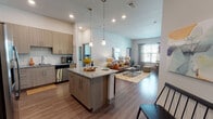 This well-appointed single-floor residence offers a thoughtfully designed open-concept layout that seamlessly connects the kitchen, dining, and living areas. The kitchen is a standout, featuring flat-front cabinetry in a warm taupe finish, granite countertops, a subway tile backsplash, and a full suite of stainless steel appliances including a refrigerator, range, microwave, and dishwasher. A center island with pendant lighting above provides additional prep space and casual dining. Rich wood-look flooring flows through the main living areas, while the spacious living room is bathed in natural light from multiple windows dressed with sheer curtains and blinds. Elevated ceilings add to the sense of openness throughout. The primary bedroom includes a walk-in closet and an en-suite bathroom with a granite-topped double vanity and a separate shower. The secondary bedroom features sliding glass doors that open directly onto a private balcony. A second full bathroom offers a tub-shower combination with tile surround, granite vanity, and large mirror. Clean lines, neutral tones, and quality finishes throughout give this residence a polished, contemporary feel.