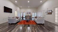 This single-floor amenity space offers a thoughtfully designed layout across a generous footprint, blending comfort and functionality throughout. Dark hardwood flooring runs continuously through all areas, creating a cohesive and polished aesthetic.

The centerpiece of the space is a bright, open lounge area with soaring ceilings, recessed lighting, and multiple large windows fitted with white shutters that invite abundant natural light. Comfortable gray sofas, a bold orange area rug, and decorative accents give this gathering area a welcoming, contemporary feel. French doors with glass pane inserts connect the lounge to a dedicated business center, which features workstations with computers, a printer, and a dining-height table with seating — ideal for work or meetings.

A compact kitchenette offers dark cabinetry, granite-style countertops, a center island, a full-size refrigerator, and a microwave, providing convenient refreshment options. The fitness center is well-equipped with cardio machines including a treadmill and elliptical, a cable weight machine, stability balls, and ample open floor space. A separate windowed room within the fitness area accommodates additional equipment. Two bathrooms and a connecting hallway complete the layout, ensuring full functionality for residents or guests using the space.