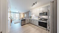 Located at 301 S Maple St in Mount Prospect, Illinois, this thoughtfully designed single-floor residence offers a seamless blend of modern finishes and warm architectural detail. The open-concept living and kitchen area serves as the heart of the space, where light wood-style flooring flows throughout and connects each zone cohesively. A striking exposed brick accent wall anchors the living area, providing rich texture and character that contrasts beautifully with the clean white walls and contemporary furnishings.

The kitchen is well-appointed with sleek gray cabinetry accented by matte black hardware, quartz countertops, a herringbone tile backsplash, and a full suite of stainless steel appliances including a gas range, over-the-range microwave, dishwasher, and a French door refrigerator. A peninsula counter extends toward the living area, reinforcing the open flow between spaces.

The bedroom is bathed in natural light through floor-to-ceiling windows with access to a private balcony, offering views of the surrounding neighborhood. The bathroom features light wood-style flooring, a gray vanity with a framed mirror, a glass-enclosed walk-in shower with white subway tile, and clean, neutral finishes throughout. Track lighting and thoughtful details complete this well-designed residence.