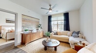 Located in Dripping Springs, TX, this well-appointed two-bedroom, three-bathroom single-floor residence offers a thoughtfully designed layout with modern finishes throughout. The open-concept living, dining, and kitchen area serves as the heart of the home, bathed in natural light from large windows dressed with elegant drapes. The living room features vaulted ceilings with a ceiling fan and warm, neutral tones complemented by wood-look flooring. The kitchen is outfitted with light wood cabinetry, white quartz countertops, a subway tile backsplash, a central island, and a full suite of stainless steel appliances. The sun-filled dining area accommodates a round table and benefits from wraparound windows that create an airy, inviting atmosphere. The primary bedroom is a comfortable retreat with a ceiling fan, generous natural light, and access to a spacious walk-in closet with built-in shelving and ample hanging storage. Three bathrooms provide convenience for residents and guests alike. Additional highlights include a dedicated in-unit laundry room with washer and dryer hookups and cabinetry, a pantry, a utility room, and a private patio with railing that overlooks the surrounding community. Two closets offer abundant storage throughout.