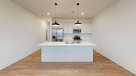 This two-story, 1-bedroom, 1-bathroom residence offers a thoughtfully designed layout spread across two levels, with the majority of the living space situated on the main floor. The open-concept kitchen serves as the centerpiece of the home, showcasing white shaker-style cabinetry, a herringbone tile backsplash, stainless steel appliances including a French door refrigerator, microwave, and range, and a large central island with a built-in sink and pendant lighting. Light hardwood-style flooring flows throughout the main living areas, complemented by recessed lighting that creates a bright, clean ambiance. A separate room on the main floor features the same hardwood-style flooring and a window that invites natural light, offering flexible use as a living or flex space. The generously sized primary bedroom is carpeted for comfort and includes a ceiling fan, a closet for storage, and a window with exterior views. The full bathroom features a clean, all-white tub and shower combination with chrome fixtures. A hallway and staircase connect the two levels, ensuring efficient circulation throughout the home. Crisp white walls and consistent finishes throughout lend the space a modern, move-in-ready aesthetic.
