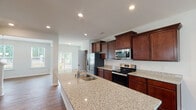 Located at 102 Spaniel Dr in Clayton, NC, this three-story home offers a thoughtfully designed layout spread across multiple levels. The kitchen serves as a functional centerpiece, showcasing rich dark wood cabinetry, granite countertops, a large island with a double sink, and a full suite of stainless steel appliances including a refrigerator, electric range, and built-in microwave. Hardwood-style flooring runs throughout the main living areas, contributing to a warm and cohesive aesthetic, while a sliding glass door allows natural light to pour in and provides outdoor access. The bedrooms feature plush carpeting and generous walk-in closets with built-in shelving, offering ample storage. The bathrooms are finished with tile flooring, warm wood vanities, and full soaking tubs. A dedicated laundry room with side-by-side washer and dryer hookups and overhead shelving adds practical convenience. The attached garage provides substantial vehicle and storage space, complete with an electrical panel and water heater. Overall, the home presents a clean, move-in-ready interior with consistent finishes throughout all three floors.
