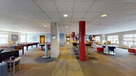 Located at 117 Washington Ave in Schenectady, NY, this single-floor community amenity space is thoughtfully designed to serve as a dynamic hub for recreation and socializing. The expansive open floor plan is anchored by striking red mosaic-tiled columns that add a bold architectural accent throughout the main gathering area.

The game room is a standout feature, housing multiple full-size pool tables with red felt, a foosball table, and arcade gaming options, all illuminated by recessed and track lighting. Adjacent to the game area is a comfortable lounge with leather seating and a flat-screen TV, decorated with colorful contemporary artwork.

A well-appointed communal kitchen serves as a central feature, complete with warm wood cabinetry, dark granite countertops, a large island with bar-height seating, a gas cooktop beneath a stainless steel range hood, dual wall-mounted TVs, and stainless steel appliances throughout. A secondary kitchen area provides additional prep space with tile flooring and natural light from exterior-facing windows.

Flexible seating zones include high-top bar tables with yellow and navy stools, as well as a bright lounge corner furnished with vibrant red ottomans and large windows that invite natural light. The space is finished with patterned carpet tiles throughout, creating a cohesive and energetic atmosphere ideal for community engagement.