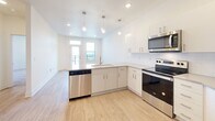 Located at 110 W Hillsdale St in downtown Lansing, Michigan, this single-floor unit offers a clean, modern design with an open and functional layout. The kitchen is a standout feature, outfitted with crisp white cabinetry, a subway tile backsplash, light wood-tone flooring, and a full suite of stainless steel appliances including a refrigerator with water dispenser, electric range, over-the-range microwave, and dishwasher. A peninsula with pendant lighting connects the kitchen to the living area, which is bathed in natural light from large windows with views of the surrounding neighborhood. The bedrooms feature plush carpeting and are thoughtfully connected via interior hallways, with one bedroom offering a window with an outdoor view. The bathroom is well-appointed with white cabinetry, a wide vanity with a large mirror, a combination tub and shower, and wood-tone flooring that complements the rest of the unit. A walk-in closet is conveniently accessible from the kitchen area, adding practical storage. Throughout the unit, recessed lighting, white panel doors, and a neutral color palette create a bright, cohesive, and move-in-ready living environment.