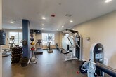 Located at 2600 Westhollow Drive in Houston, TX, this fitness center offers a well-organized and fully equipped workout facility across a single floor. The gym features durable rubber flooring throughout, recessed lighting in a clean white ceiling, and neutral-toned walls accented by a bold blue structural column that adds a distinct visual element to the space.

Large windows along the exterior wall invite natural light and provide views of the surrounding outdoor area, creating a bright and energizing atmosphere. Full-length mirrors are installed along one wall, visually expanding the space and allowing users to monitor their form during workouts.

The cardio section is equipped with treadmills, elliptical trainers, and a stepper, while the strength training area features multiple cable and weight machines, including Instinct-brand equipment. A dedicated free weights section includes a rack of dumbbells and a collection of medicine balls, catering to a variety of training styles. An additional resistance/bench press machine rounds out the strength offerings.

Safety features include a fire sprinkler system and a mounted fire extinguisher. A door leads to an adjacent bathroom, providing added convenience. The layout is thoughtfully arranged to maximize usability and flow, making this fitness center a comprehensive and functional amenity.