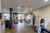 Located at 2600 Westhollow Drive in Houston, TX, this fitness center offers a well-organized and fully equipped workout facility across a single floor. The gym features durable rubber flooring throughout, recessed lighting in a clean white ceiling, and neutral-toned walls accented by a bold blue structural column that adds a distinct visual element to the space.

Large windows along the exterior wall invite natural light and provide views of the surrounding outdoor area, creating a bright and energizing atmosphere. Full-length mirrors are installed along one wall, visually expanding the space and allowing users to monitor their form during workouts.

The cardio section is equipped with treadmills, elliptical trainers, and a stepper, while the strength training area features multiple cable and weight machines, including Instinct-brand equipment. A dedicated free weights section includes a rack of dumbbells and a collection of medicine balls, catering to a variety of training styles. An additional resistance/bench press machine rounds out the strength offerings.

Safety features include a fire sprinkler system and a mounted fire extinguisher. A door leads to an adjacent bathroom, providing added convenience. The layout is thoughtfully arranged to maximize usability and flow, making this fitness center a comprehensive and functional amenity.