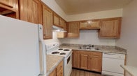 This single-floor unit at Royal Arms offers a practical and comfortable layout designed for everyday living. The kitchen is equipped with warm honey-toned oak cabinetry providing ample storage above and below the counters. Laminate countertops, a double-basin stainless steel sink, a coil-burner electric range, and a dishwasher complete the functional setup. A pass-through opening connects the kitchen to the main living area, enhancing the open feel and allowing natural light to flow between spaces. A pendant light accents this pass-through bar, adding a subtle design touch.

The living area is generously sized, featuring plush wall-to-wall carpeting and a large sliding glass door fitted with vertical blinds, inviting natural light and offering outdoor views. The bedrooms are similarly carpeted, finished in neutral tones, and include windows for additional natural light.

The bathrooms feature wood-look plank flooring, white vanities with integrated sinks, mirrored medicine cabinets, and a full soaking tub with shower. The overall aesthetic throughout the unit is clean and neutral, with textured ceilings, white trim, and a cohesive, understated palette that provides a versatile foundation for any décor style.