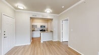 This 2-bedroom, 1-bathroom single-floor unit offers a well-organized layout with consistent light hardwood-style flooring and neutral warm beige tones throughout. The open-concept living area connects seamlessly to the kitchen, which is equipped with white shaker-style cabinetry, granite countertops, a stainless steel dishwasher, range, and microwave, along with a peninsula that provides additional workspace and casual dining potential. Crown molding accents the living and bedroom areas, adding a refined architectural detail to the overall design.

The primary bedroom offers a comfortable footprint with a ceiling fan, natural light from large windows fitted with blinds, and access to a closet. The second bedroom is similarly appointed with neutral walls and hardwood-style flooring. A sun-filled nook with a wall of windows provides an airy transition between rooms, allowing ample natural light to fill the space.

The full bathroom features a granite-topped vanity with white cabinetry, a tiled tub-shower combination, and hardwood-style flooring that maintains continuity with the rest of the unit. Additional functional spaces include a dedicated laundry area and a closet. The unit's clean, light-filled interior and cohesive finishes create a practical and comfortable living environment.