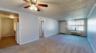 Located at 460 E Dayton Yellow Springs Rd in Fairborn, Ohio, this one-bedroom, one-bathroom unit offers a practical and comfortable single-floor layout. The living room is a generous, open space anchored by a ceiling fan with light fixture and soft carpeting underfoot. A standout feature is the built-in wall unit with arched shelving and cabinet storage, providing both display space and functional organization. Natural light enters through a window alongside the entry door, which also houses a wall-mounted HVAC unit. The bedroom is a well-proportioned retreat with its own ceiling fan, carpeted flooring, and a closet, with a view to an additional closet space beyond. A window with blinds allows natural light and outdoor views. The kitchen features wood-toned cabinetry, light countertops, and wood-style flooring, with a dedicated pantry offering open shelving for additional storage. The bathroom includes a wood-toned vanity with a wide white countertop, a single-basin sink, a medicine cabinet mirror with overhead lighting, and wood-style flooring. A hallway connects the rooms cohesively. Textured ceilings are consistent throughout the unit, lending a classic residential character to the space.