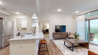 Located in Dripping Springs, TX, this single-floor residence offers a thoughtfully designed layout that balances comfort and functionality. The open-concept living and kitchen area serves as the heart of the home, featuring wood-look flooring, crown molding, and recessed lighting throughout. The kitchen is outfitted with white cabinetry, granite countertops, stainless steel appliances, and a peninsula with bar seating — ideal for casual dining. Pendant lights add a warm, welcoming ambiance to the space.

The living room is bright and inviting, with a sliding glass door that opens to a private balcony offering green outdoor views. The bedrooms are carpeted for comfort and accented with crown molding, providing a calm and restful retreat. The primary bedroom includes a window with natural light.

The bathroom features wood-look flooring, a soaking tub with marble-style tile surround, white vanity cabinetry, and access to a walk-in closet. A dedicated laundry area with washer and dryer is conveniently located within the unit. Clean white walls and neutral tones throughout create a cohesive, modern aesthetic well-suited to the Texas Hill Country setting.