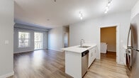 This well-designed 2-bedroom, 1-bathroom unit offers a thoughtful single-level layout with modern finishes and a clean, contemporary aesthetic. Warm-toned laminate flooring flows consistently throughout, unifying the space and complementing the crisp white walls and trim.

At the heart of the unit, the open-concept kitchen and living area form a bright, cohesive space. The kitchen features a central island with a white quartz countertop, an undermount double sink, and stainless steel appliances including a refrigerator, stove, microwave, and dishwasher. White shaker-style cabinetry extends to the ceiling, maximizing storage. Track lighting illuminates both the kitchen and living area, which opens to a private balcony offering elevated views of surrounding trees and distant mountains.

Both bedrooms are comfortably sized with large windows that invite natural light and wooded views. The primary bedroom includes a wall-mounted mini-split heating and cooling unit. The bathroom provides a wide vanity with a white countertop and a large mirror. A dedicated laundry room accommodates a full-sized front-loading washer and dryer, complete with built-in wire shelving for added storage utility.