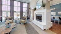 This single-story clubhouse in Canton, Michigan offers a thoughtfully designed community gathering space with a refined aesthetic throughout. The grand entrance lobby sets an impressive tone, featuring soaring ceilings, large-format tile flooring with an inlaid parquet-style accent, a decorative orb chandelier, and a central accent table. Natural light filters through tall windows flanking the entryway, illuminating the welcoming reception area and adjacent conference room.

The main lounge area showcases high ceilings with classic wainscoting, plush seating arrangements, and a striking white-surround fireplace topped with a round mirror. Floor-to-ceiling windows dressed in elegant draping provide views of the outdoor pool area, enhancing the bright, airy atmosphere.

A second lounge and game room features bold teal accent walls, hardwood-style flooring, a shuffleboard table, and a fully equipped kitchen with stainless steel appliances, white cabinetry, a large center island with pendant lighting, and bar seating. The primary kitchen area mirrors this functionality, offering a spacious white quartz island with industrial-style pendant lights and patterned upholstered bar seating, ideal for community gatherings and events.