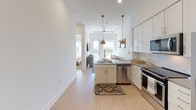 Located at 599 Harrold St in Fort Worth, Texas, this single-story residence offers a thoughtfully designed open-concept layout with clean, modern finishes and an abundance of natural light. The kitchen is a standout feature, showcasing white shaker cabinetry, a striking herringbone tile backsplash, gray quartz countertops, stainless steel appliances, and a center island with a sink — all complemented by light wood-look flooring that flows seamlessly throughout the living areas. Pendant lighting with warm brass accents adds a stylish touch above the island, while large windows at the far end of the living space frame outdoor views and flood the interior with sunlight. A ceiling fan keeps the open living and dining area comfortable year-round. The bedrooms are serene and well-proportioned, each featuring large windows with sheer curtains that invite natural light and offer pleasant outdoor views. The primary bedroom connects to a sleek en-suite bathroom appointed with white cabinetry, a wide vanity with a gray countertop, a large mirror, and a glass-enclosed walk-in shower with white subway tile. The overall aesthetic is crisp, contemporary, and inviting — a cohesive blend of comfort and modern design.