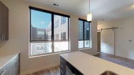 This single-floor residence at The Edge on 4th showcases a thoughtfully designed open layout with contemporary finishes throughout. The kitchen serves as a central hub of the space, featuring a large island with a white quartz countertop, an undermount sink, and pendant lighting overhead. Sleek, wood-toned cabinetry extends floor to ceiling along the kitchen wall, complemented by a white subway tile backsplash and a full suite of stainless steel appliances. Durable wood-look flooring runs throughout the main living and kitchen areas, adding warmth to the modern aesthetic.

Large windows in the kitchen and adjoining living areas invite abundant natural light while offering views of the surrounding urban streetscape. A distinctive sliding barn door adds a stylish architectural detail, connecting living spaces with functional flair. The bedrooms are carpeted for comfort, each equipped with ceiling fans and ample room for furnishings. One bedroom features a generous walk-in closet with multiple hanging rods and shelving.

The bathroom is well-appointed with a dual-sink vanity, dark wood cabinetry, white countertops, framed mirrors, and wood-look flooring, creating a clean and cohesive design. Throughout the residence, neutral tones and modern fixtures establish a polished, move-in-ready ambiance.