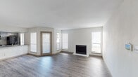 This single-floor residence offers a clean, modern aesthetic throughout, with light neutral walls and durable wood-look flooring that flows seamlessly across the main living areas. The spacious living room is a standout feature, anchored by a crisp white fireplace and bathed in natural light from multiple windows fitted with horizontal blinds. A glass-paneled exterior door provides convenient outdoor access directly from the living space, enhancing the open, airy feel of the room.

The kitchen is practical and well-designed, featuring gray stone-look countertops, a stainless steel sink, and a stainless steel refrigerator. A pass-through counter connects the kitchen to the adjacent dining or living area, promoting an open flow throughout the home. Generous windows in the kitchen area flood the space with additional natural light.

The bedroom is a comfortable, well-proportioned room with the same wood-look flooring, a ceiling fan with lighting, and a window for natural light and ventilation.

The bathroom is thoughtfully appointed with gray shaker-style cabinetry, a gray countertop vanity, dual mirrors, brushed nickel fixtures, and ample overhead cabinet storage. A separate tub and shower combination with a curved curtain rod and brushed nickel hardware completes the bathroom. Clean white walls and warm wood-look flooring tie the space together with a cohesive, contemporary style.