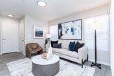 Located at 7400 S State St in Midvale, Utah, this thoughtfully designed one-bedroom, one-bathroom residence offers a cohesive modern aesthetic throughout its single-floor layout. Light wood-style flooring flows seamlessly from room to room, complemented by a neutral color palette that creates a clean, airy ambiance.

The living room is a welcoming focal point, featuring multiple windows with slatted blinds that invite natural light, along with a sliding glass door that opens to an outdoor view. The space comfortably accommodates a full seating arrangement and transitions naturally into the dining area, where a bay-style window configuration with a ceiling fan adds architectural charm and further brightens the room.

The galley-style kitchen is efficiently organized with white upper cabinetry, gray lower cabinets, white quartz-style countertops, and a full suite of stainless steel appliances, including a refrigerator, range, microwave, and dishwasher. It connects directly to a dedicated laundry area fitted with a full-size top-loading washer and dryer alongside built-in shelving.

The bedroom is generously proportioned with access to a walk-in closet. The bathroom features wood-look tile flooring, a gray vanity with a white countertop, a well-lit mirror, and a shower/tub combination. A hallway connects the private spaces, completing this practical and stylish single-level home.