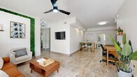 Located in the heart of Cocoa Beach, Florida, this well-appointed 2-bedroom, 2-bathroom single-story home offers a comfortable and cohesive layout designed for easy living. Travertine-style tile flooring runs throughout the entire home, lending a clean, cohesive aesthetic to every room.

The open living area is a standout feature, highlighted by a striking green botanical wall accent, crown molding, and a ceiling fan overhead. Natural light filters in through large windows dressed with sheer curtains. The living space flows seamlessly into the dining area, which is anchored by a casual bar-height table, and into the fully equipped kitchen. The kitchen features stainless steel appliances, dark granite countertops, white upper cabinetry, and a tray ceiling with recessed lighting.

Both bedrooms are generously sized, each featuring ceiling fans, crown molding, closets, and large windows that fill the rooms with natural light. A tropical palm motif carries through the decor, reinforcing the coastal ambiance.

The two bathrooms include a sleek glass-enclosed walk-in shower with floor-to-ceiling tile. A dedicated laundry room houses a full-size washer and dryer alongside overhead cabinetry for storage. Outdoor spaces include a patio and balcony, complemented by lush palm tree surroundings and ample parking.