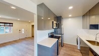 This single-floor unit showcases a clean, modern design with consistent light wood-tone flooring and crisp white walls throughout, creating a bright and cohesive aesthetic. Recessed lighting is installed in every room, ensuring well-distributed illumination across the entire space.

The open living area is generously proportioned, featuring a large window with a stylish roman shade that allows ample natural light while offering views of the surrounding neighborhood. The front entry door includes a modern smart lock and glass panel accents.

The kitchen is a standout feature, designed in a galley layout with high-gloss gray cabinetry extending nearly to the ceiling for maximum storage. Sleek white quartz countertops run along both sides, complemented by stainless steel appliances including a range, over-the-range microwave, refrigerator, and dishwasher. A modern undermount sink with a pull-down faucet completes the functional workspace.

The unit includes two bedrooms, each with recessed lighting, closet storage with sliding or hinged doors, and windows that bring in natural light. One bedroom features a wall-mounted air conditioning unit.

The bathroom is finished with large-format gray marble-look wall tiles in a glass-enclosed walk-in shower, white tile flooring, and a floating vanity, delivering a clean, contemporary feel.
