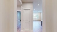 Located at 15228 Statesville Rd in Huntersville, NC, this well-appointed 1-bedroom, 2-bathroom residence offers a thoughtfully designed single-level layout. The open-concept kitchen and living area serves as the heart of the home, showcasing white shaker cabinetry extending to the ceiling, stainless steel appliances including a French door refrigerator and range, a white quartz countertop island with a contrasting grey base, and pendant lighting. Light hardwood flooring flows throughout the main living areas, creating a warm and cohesive aesthetic. The spacious primary bedroom features multiple windows that invite abundant natural light and a ceiling fan, with a dedicated closet providing ample storage. The two bathrooms are finished with a clean, modern palette — one highlights a glass-enclosed walk-in shower with floor-to-ceiling tile, a built-in bench, and mosaic tile flooring, paired with a white vanity and matte black hardware accents. A covered balcony extends the living space outdoors, offering views of surrounding greenery. The entrance and hallway provide a clean transition through the home, completing this functional and stylish residence.