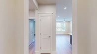 Located at 15228 Statesville Rd in Huntersville, NC, this well-appointed 1-bedroom, 2-bathroom residence offers a thoughtfully designed single-level layout. The open-concept kitchen and living area serves as the heart of the home, showcasing white shaker cabinetry extending to the ceiling, stainless steel appliances including a French door refrigerator and range, a white quartz countertop island with a contrasting grey base, and pendant lighting. Light hardwood flooring flows throughout the main living areas, creating a warm and cohesive aesthetic. The spacious primary bedroom features multiple windows that invite abundant natural light and a ceiling fan, with a dedicated closet providing ample storage. The two bathrooms are finished with a clean, modern palette — one highlights a glass-enclosed walk-in shower with floor-to-ceiling tile, a built-in bench, and mosaic tile flooring, paired with a white vanity and matte black hardware accents. A covered balcony extends the living space outdoors, offering views of surrounding greenery. The entrance and hallway provide a clean transition through the home, completing this functional and stylish residence.
