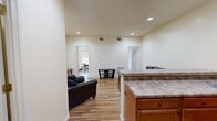 Located at 1067 Philadelphia St in Indiana, PA, this single-floor, 3-bedroom, 1-bathroom unit offers a practical and well-appointed layout. The open-concept kitchen and living area serves as the heart of the space, featuring warm hardwood-style flooring, recessed lighting, and neutral wall tones throughout. The kitchen is equipped with warm wood cabinetry, granite-style countertops, black appliances including a refrigerator, electric range, and microwave, along with a breakfast bar with barstool seating. The adjoining living area provides a comfortable gathering space with room for seating and a media console. Three bedrooms are efficiently arranged off the main living area, each featuring the same hardwood-style flooring, windows with exterior views, and clean, neutral walls that offer a blank canvas for personalization. The primary bedroom provides a modest yet functional space. The shared full bathroom is a standout feature, offering a dual-sink vanity with wood cabinetry, white countertops, and full-width mirrors illuminated by overhead lighting. The consistent finishes and thoughtful layout make this a well-designed, functional unit suited for everyday living.