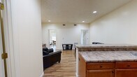 Located at 1067 Philadelphia St in Indiana, PA, this single-floor, 3-bedroom, 1-bathroom unit offers a practical and well-appointed layout. The open-concept kitchen and living area serves as the heart of the space, featuring warm hardwood-style flooring, recessed lighting, and neutral wall tones throughout. The kitchen is equipped with warm wood cabinetry, granite-style countertops, black appliances including a refrigerator, electric range, and microwave, along with a breakfast bar with barstool seating. The adjoining living area provides a comfortable gathering space with room for seating and a media console. Three bedrooms are efficiently arranged off the main living area, each featuring the same hardwood-style flooring, windows with exterior views, and clean, neutral walls that offer a blank canvas for personalization. The primary bedroom provides a modest yet functional space. The shared full bathroom is a standout feature, offering a dual-sink vanity with wood cabinetry, white countertops, and full-width mirrors illuminated by overhead lighting. The consistent finishes and thoughtful layout make this a well-designed, functional unit suited for everyday living.