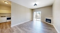 This well-appointed one-bedroom, one-bathroom unit in Gladstone, Oregon offers a thoughtfully designed layout across a single floor. The open-concept living and kitchen area serves as the heart of the home, featuring warm wood-toned cabinetry, granite countertops, a peninsula island with a stainless steel sink, and a full suite of stainless steel appliances including a refrigerator, range, and microwave. Durable hardwood-style flooring runs throughout the kitchen and living areas, adding a clean, modern feel. The living room is highlighted by a corner fireplace with a white mantle and a sliding glass door that opens to a private balcony, filling the space with natural light and offering outdoor views. The bedroom is comfortably sized, featuring plush carpeting, a ceiling fan, and a window that brings in additional natural light. The full bathroom includes a tub/shower combination, wood-toned vanity with granite countertops, and hardwood-style flooring. A dedicated in-unit laundry area with a full-size washer and dryer adds everyday convenience. Neutral tones and clean finishes throughout create a cohesive, inviting ambiance.