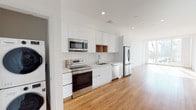 Located at 250 S Kenmore Ave in the heart of Los Angeles, this modern single-floor unit showcases a clean, contemporary design throughout. Warm hardwood flooring flows seamlessly across the open-plan living areas, complementing the crisp white walls and recessed lighting that give the space a bright, airy feel.

The kitchen is a standout feature, equipped with full stainless steel appliances including a range, microwave, dishwasher, and refrigerator. Sleek, high-gloss white cabinetry extends to the ceiling, maximizing storage, while a classic white subway tile backsplash and light quartz countertops add refined detail. A warm wood open-shelf accent provides a touch of natural contrast.

The living areas are generously proportioned, anchored by expansive floor-to-ceiling windows and sliding glass doors that flood the space with natural light and offer open views of the surrounding Los Angeles neighborhood, including sweeping sightlines of palm tree-lined streets. A private balcony extends the living space outdoors.

The bathroom is finished with white penny-tile flooring, subway-tiled walls, a combined soaking tub and shower with a glass enclosure, and brushed nickel fixtures. Throughout the unit, the design balances modern minimalism with functional, high-quality materials, creating a cohesive and inviting living environment.