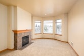 This well-appointed single-floor residence offers a thoughtfully designed layout that balances comfort and functionality throughout. The spacious living room serves as the heart of the home, anchored by a classic tile-surround fireplace with a warm wood mantle and framed by a sweeping bay window that fills the room with natural light and offers pleasant outdoor views. Plush wall-to-wall carpeting extends throughout the living areas and bedrooms, lending a cozy, uniform feel to the space.

The kitchen features warm honey-toned wood cabinetry, light countertops, and a raised breakfast bar that opens to the main living area, creating an inviting, connected atmosphere. Recessed lighting above the kitchen adds a clean, modern touch. Adjacent to the kitchen is a utility area with matching cabinetry and hardwood-style flooring, providing practical storage and workspace.

The bedrooms are generously sized, each with soft carpeting and ample natural light. One bedroom features a sliding glass door that opens to a private balcony with outdoor views, while another includes a full-width sliding closet. The bathroom is equipped with a full-size soaking tub and shower combination, complemented by neutral tones and hardwood-style flooring. Throughout the space, warm wood trim and soft neutral tones create a cohesive and welcoming ambiance.