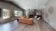 Located in Lakewood, Washington, this single-story community clubhouse offers a thoughtfully designed gathering space blending modern aesthetics with functional amenities. The main lounge area features vaulted ceilings, warm hardwood-style flooring, and a striking floor-to-ceiling dark tile fireplace that serves as a dramatic focal point. A large picture window floods the space with natural light, while a statement pendant light and recessed lighting complete the ambiance. Comfortable leather seating and eclectic accent chairs create an inviting atmosphere for socializing or relaxing. The fully equipped kitchen is a standout feature, showcasing a bold teal island with an expansive stone countertop, natural wood cabinetry, large-format tile backsplash, stainless steel appliances, and eye-catching copper-toned pendant lights. Bar seating along the island makes it ideal for casual gatherings. The game room is a lively retreat with soaring ceilings accented by exposed wood beams, a vibrant teal accent wall, a full-size pool table, shuffleboard table, mounted flat-screen TV, and a wall of glass garage-style doors that open to an outdoor area. Together, these spaces deliver a dynamic, well-appointed clubhouse experience.