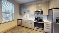Located at 411 W Hargett St in the heart of downtown Raleigh, North Carolina, this single-floor unit offers a thoughtfully designed open layout finished with contemporary details throughout. Wood-look flooring extends across the main living areas, complementing the neutral gray and white color palette that lends the space a clean, modern aesthetic.

The living area is generously proportioned, with ceiling fans providing both function and visual interest. Track lighting adds a modern touch, while windows along the exterior wall allow natural light to filter in, creating a bright and welcoming atmosphere.

The kitchen is well-appointed, featuring light wood-toned cabinetry that reaches toward the ceiling for ample storage, paired with a white subway tile backsplash and light quartz countertops. Stainless steel appliances — including a range, over-the-range microwave, dishwasher, and refrigerator — provide a polished, functional workspace. A single-basin sink with a contemporary faucet completes the setup.

The bathroom showcases a walk-in glass-enclosed shower finished with white subway tile walls, brushed nickel fixtures, and matte black hardware accents. Multiple interior doors, visible along a central hallway, indicate well-defined room separation, providing privacy and efficient use of the floor plan throughout the unit.