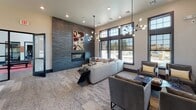 This contemporary community clubroom is thoughtfully designed to offer both comfort and functionality in a single, open-plan space. Soaring ceilings amplify the sense of openness, while large, dark-framed windows lining the walls flood the interior with abundant natural light and provide views to the outdoors.

The lounge area serves as the centerpiece of the space, anchored by a striking floor-to-ceiling dark slate accent wall housing a sleek linear fireplace. A bold piece of abstract artwork above the fireplace adds a vibrant pop of color against the muted tones of the surrounding décor. Plush sectional sofas and upholstered lounge chairs are arranged thoughtfully around coffee tables, creating an inviting atmosphere for relaxation and socializing. The space is illuminated by dramatic sputnik-style chandeliers that serve as stylish focal points.

Adjacent to the lounge, a billiards table offers a recreational element, positioned near the glass-paned entryway doors that reinforce the space's modern industrial aesthetic. On the opposite side, a dedicated media and seating nook features a wall-mounted flat-screen TV, accompanied by comfortable armchairs and accent lighting via track fixtures.

A built-in business center with workstations and pendant lighting provides a productive corner for residents. Textured carpet flooring with a geometric pattern runs throughout, tying the distinct zones together into a cohesive, well-appointed communal environment.