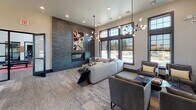 This contemporary community clubroom is thoughtfully designed to offer both comfort and functionality in a single, open-plan space. Soaring ceilings amplify the sense of openness, while large, dark-framed windows lining the walls flood the interior with abundant natural light and provide views to the outdoors.

The lounge area serves as the centerpiece of the space, anchored by a striking floor-to-ceiling dark slate accent wall housing a sleek linear fireplace. A bold piece of abstract artwork above the fireplace adds a vibrant pop of color against the muted tones of the surrounding décor. Plush sectional sofas and upholstered lounge chairs are arranged thoughtfully around coffee tables, creating an inviting atmosphere for relaxation and socializing. The space is illuminated by dramatic sputnik-style chandeliers that serve as stylish focal points.

Adjacent to the lounge, a billiards table offers a recreational element, positioned near the glass-paned entryway doors that reinforce the space's modern industrial aesthetic. On the opposite side, a dedicated media and seating nook features a wall-mounted flat-screen TV, accompanied by comfortable armchairs and accent lighting via track fixtures.

A built-in business center with workstations and pendant lighting provides a productive corner for residents. Textured carpet flooring with a geometric pattern runs throughout, tying the distinct zones together into a cohesive, well-appointed communal environment.