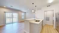 Located on Longs Peak Street in Brighton, Colorado, this one-bedroom, one-bathroom unit offers a thoughtfully designed open-concept layout finished with contemporary touches throughout. Light wood-style flooring runs through the main living areas, creating a clean, cohesive aesthetic. The kitchen serves as the heart of the space, featuring a central island with a stainless steel sink, crisp white quartz countertops, shaker-style cabinetry, a subway tile backsplash, and a full suite of stainless steel appliances including a range, microwave, and refrigerator. Stylish pendant lights hang above the island, adding a modern accent. A dedicated laundry alcove with stacked washer and dryer units is conveniently tucked just off the kitchen. The living area is bright and open, highlighted by a sliding glass door with vertical blinds that leads to an outdoor balcony, inviting abundant natural light and exterior views. The bedroom is carpeted for comfort, features a ceiling fan, and includes a dedicated closet. The bathroom is well-appointed with gray shaker vanity cabinets, a white countertop, a framed mirror, and a bathtub. A hallway connects all areas efficiently, completing this well-organized and modern single-floor residence.