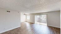 This single-story, 2-bedroom, 1-bathroom residence in Mesa, Arizona offers a practical and well-organized layout across a comfortable footprint. Wood-look flooring runs consistently throughout the unit, lending warmth and visual continuity to every room.

The combined living room and kitchen area forms the central hub of the home. The living room is bright and open, benefiting from a ceiling fan, a large sliding glass door fitted with vertical blinds, and an adjacent window that together invite abundant natural light and views of outdoor greenery. The galley-style kitchen features white cabinetry, dark laminate countertops, a stainless steel sink, and black appliances including a range, microwave, and refrigerator, all illuminated by overhead flush-mount lighting.

Both bedrooms are finished with the same wood-look flooring and textured ceilings. The primary bedroom includes a built-in closet with a hanging rod and a window with vertical blinds. The secondary bedroom is a well-proportioned space with natural light from an exterior window. A hallway connects the bedrooms to the shared full bathroom, which features a white vanity with a gray countertop, a mirror, and a tub-shower combination with a chrome fixture.