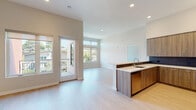 This single-floor residence showcases a contemporary design with a clean, neutral palette and thoughtful finishes throughout. The open-concept living and kitchen area is anchored by light hardwood-style flooring, soaring ceilings, and an abundance of natural light streaming through large windows and a glass-panel door leading to a private balcony.

The kitchen is a standout feature, equipped with warm wood-grain cabinetry extending to ceiling height, crisp white countertops, a dark tile backsplash, and a full suite of stainless steel appliances including a French-door refrigerator, range, and over-the-range microwave. A peninsula with an integrated sink provides additional prep space and casual seating potential, seamlessly connecting the kitchen to the open living area.

The bedrooms are carpeted for comfort, each offering generous proportions and ample natural light. Walk-in closets with built-in shelving and hanging rods provide practical storage solutions. The primary bathroom features a glass-enclosed walk-in shower with large-format tile and direct access to its walk-in closet. A secondary full bathroom includes a single-sink vanity with wood cabinetry, a mirror, and a bathtub combination, finished with the same light hardwood-style flooring found throughout the main living spaces.