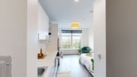 Unit 404 at 1617 Market St in Tacoma, Washington, is a thoughtfully designed studio offering a bright, open-plan layout with a clean, modern aesthetic. Light-toned wood-style flooring and crisp white walls run throughout, creating a cohesive and airy atmosphere. A large picture window anchors the living area, flooding the space with natural light and framing expansive views of the surrounding Tacoma cityscape and treetops beyond.

The kitchen is efficiently arranged along one wall, featuring white flat-front cabinetry with open shelving, a stainless steel refrigerator, an induction cooktop with a pull-out drawer, a microwave, and a single-basin sink — providing all essential appliances in a compact, well-organized footprint. The sleeping area sits adjacent to the kitchen, with ample room for a full-sized bed and a seating area near the window.

The bathroom is finished in soft neutral tones with wood-style flooring, a white vanity with an undermount sink, a toilet, and a shower-tub combination with a curtain rod. A warm flush-mount ceiling fixture with a yellow shade adds a pop of character to the main living space, complementing the otherwise minimalist design. This unit offers a practical and polished urban living environment in the heart of Tacoma.