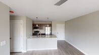 This well-appointed single-floor residence showcases a clean, contemporary design throughout. The open-concept living and kitchen area serves as the heart of the home, featuring light wood-look flooring, neutral wall tones, and a seamless flow between spaces. The kitchen is equipped with stainless steel appliances — including a refrigerator, range, and over-the-range microwave — complemented by rich dark cabinetry and a large white quartz island with an undermount sink. Pendant lighting above the island adds a stylish, functional touch. The living area extends to a sliding glass door that opens onto a private balcony, offering pleasant outdoor views and abundant natural light. Multiple bedrooms are carpeted for comfort, each featuring modern ceiling fans, large windows that bring in natural light, and views of the surrounding landscape. The unit includes two full bathrooms: one with a tub-shower combination, dark wood vanity, and dark wood flooring, and a second featuring a dual-sink vanity with quartz countertops, a large mirror, light wood flooring, and a separate shower. The consistent use of neutral tones, modern fixtures, and quality finishes creates a cohesive and inviting atmosphere throughout the entire space.