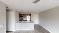 This well-appointed single-floor residence showcases a clean, contemporary design throughout. The open-concept living and kitchen area serves as the heart of the home, featuring light wood-look flooring, neutral wall tones, and a seamless flow between spaces. The kitchen is equipped with stainless steel appliances — including a refrigerator, range, and over-the-range microwave — complemented by rich dark cabinetry and a large white quartz island with an undermount sink. Pendant lighting above the island adds a stylish, functional touch. The living area extends to a sliding glass door that opens onto a private balcony, offering pleasant outdoor views and abundant natural light. Multiple bedrooms are carpeted for comfort, each featuring modern ceiling fans, large windows that bring in natural light, and views of the surrounding landscape. The unit includes two full bathrooms: one with a tub-shower combination, dark wood vanity, and dark wood flooring, and a second featuring a dual-sink vanity with quartz countertops, a large mirror, light wood flooring, and a separate shower. The consistent use of neutral tones, modern fixtures, and quality finishes creates a cohesive and inviting atmosphere throughout the entire space.