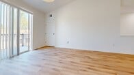 This contemporary 1-bedroom apartment offers 790 square feet of thoughtfully designed living space. The open-concept layout seamlessly integrates the living room and kitchen, creating an airy and spacious atmosphere. The kitchen boasts sleek white cabinetry, stainless steel appliances, and a convenient island with a sink, perfect for casual dining or entertaining.

The bedroom, measuring 140 square feet, features large windows that flood the space with natural light and provide picturesque views. Hardwood floors run throughout the apartment, adding warmth and elegance to the modern design. The bathroom is well-appointed with a vanity, toilet, and a glass-enclosed shower.

A standout feature is the private balcony, accessible from the living area, offering outdoor space and views of the surrounding property. The apartment's crisp white walls and high ceilings enhance the sense of openness and brightness.

Located in a newer development, residents benefit from on-site amenities such as storage units and ample parking. The property's landscaped grounds and neighboring structures suggest a pleasant, community-oriented environment. This apartment combines contemporary style with practical living, making it an ideal choice for those seeking a modern, low-maintenance lifestyle.