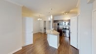 This single-floor residence offers a thoughtfully designed layout that balances comfort and functionality. Rich, dark hardwood-style flooring flows seamlessly throughout the main living areas, complementing the neutral-toned walls and crisp white trim and baseboards that frame each room.

The open-concept living area is bright and welcoming, featuring crown molding, a ceiling fan with light fixture, and access to a glass-paned exterior door that allows natural light to pour in. The space connects fluidly to the kitchen, which serves as a central hub of the home. The kitchen is equipped with dark espresso cabinetry, granite-style countertops, a center island with additional prep space, stainless steel appliances including a refrigerator, range, microwave, and dishwasher, and pendant lighting overhead that adds a refined touch.

The bedroom continues the warm flooring aesthetic and includes a ceiling fan, a window with blinds for natural light and privacy, and direct access to a closet. The bathroom features large-format tile surrounding the tub and shower area, conveying a clean and modern aesthetic. Throughout the space, the consistent use of neutral tones, quality finishes, and practical design elements create a cohesive and inviting atmosphere.