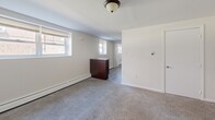 Located on Fairfield Street in Philadelphia, PA, this two-bedroom, one-bathroom unit offers a practical and efficiently organized single-floor layout. The interior is finished with neutral white walls and soft gray carpeting throughout the living and bedroom areas, creating a clean and understated aesthetic.

The spacious primary bedroom is a standout feature, offering generous room for furnishings and natural light through a double-hung window. Baseboard heating runs along the perimeter walls in multiple rooms, ensuring consistent warmth. A second bedroom provides additional flexibility, also finished with the same neutral carpet and white walls.

The open living area transitions to a functional kitchen equipped with dark wood cabinetry, a gas range, and overhead cabinetry providing ample storage. A kitchen island or counter unit adds useful workspace to the layout. The floor in the kitchen and connecting areas features hardwood-style flooring, contrasting with the carpeted rooms.

The bathroom is well-appointed with large-format neutral tile on the walls surrounding a soaking tub, accented by a decorative mosaic tile border. A wood-toned vanity completes the space. Flush-mount ceiling light fixtures are consistent throughout the unit. The entry features a solid door with secure hardware, opening into the carpeted main living space.