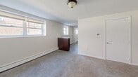 Located on Fairfield Street in Philadelphia, PA, this two-bedroom, one-bathroom unit offers a practical and efficiently organized single-floor layout. The interior is finished with neutral white walls and soft gray carpeting throughout the living and bedroom areas, creating a clean and understated aesthetic.

The spacious primary bedroom is a standout feature, offering generous room for furnishings and natural light through a double-hung window. Baseboard heating runs along the perimeter walls in multiple rooms, ensuring consistent warmth. A second bedroom provides additional flexibility, also finished with the same neutral carpet and white walls.

The open living area transitions to a functional kitchen equipped with dark wood cabinetry, a gas range, and overhead cabinetry providing ample storage. A kitchen island or counter unit adds useful workspace to the layout. The floor in the kitchen and connecting areas features hardwood-style flooring, contrasting with the carpeted rooms.

The bathroom is well-appointed with large-format neutral tile on the walls surrounding a soaking tub, accented by a decorative mosaic tile border. A wood-toned vanity completes the space. Flush-mount ceiling light fixtures are consistent throughout the unit. The entry features a solid door with secure hardware, opening into the carpeted main living space.